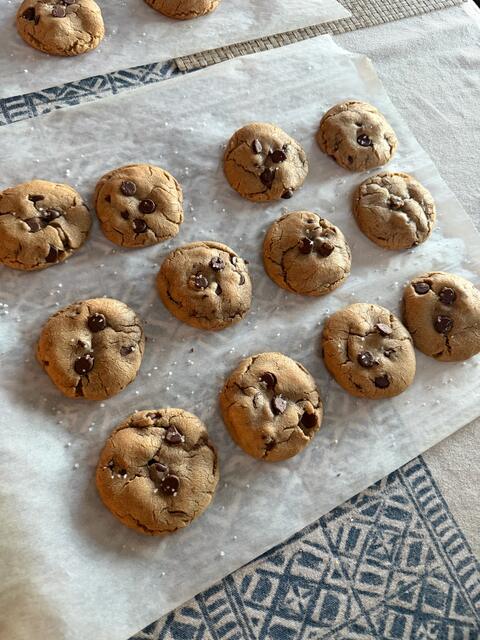 Chocolate chip cookies sprinkled with flaky sea salt, cooling on parchment paper