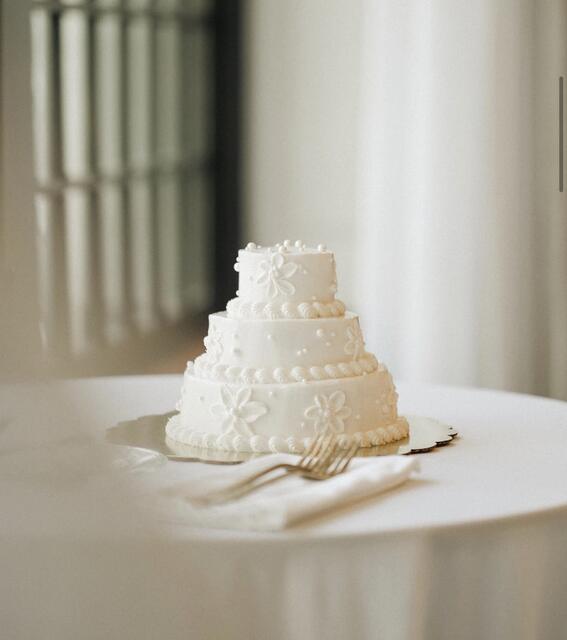 Three-tier round white wedding cake decorated with piped buttercream flowers, on a linen-draped table